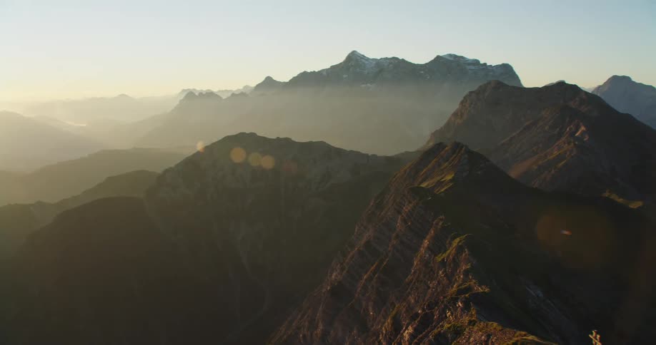Sun shines over cross standing on summit of mountain in mountain range