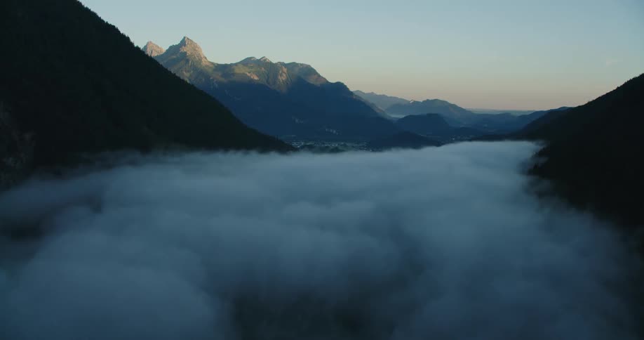 Fog lies in the valley between large tree covered mountains