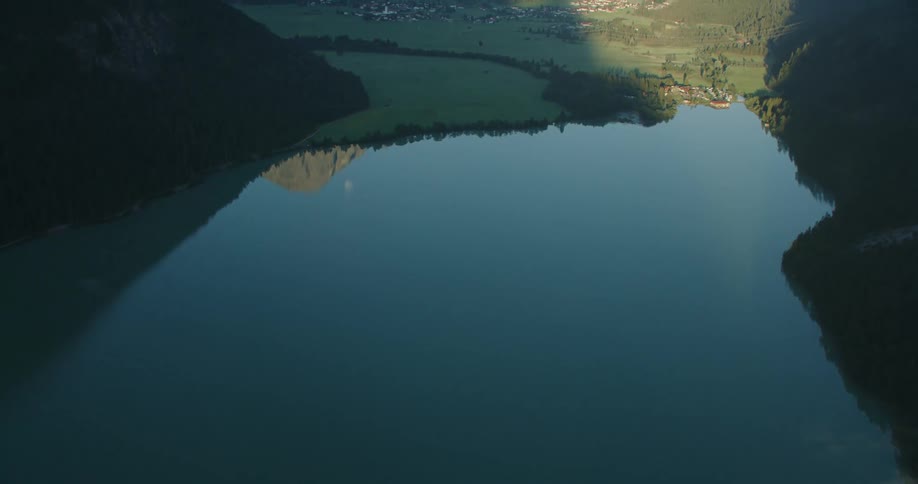 A calm lake and small town in the verdant valley of a mountain range during the day