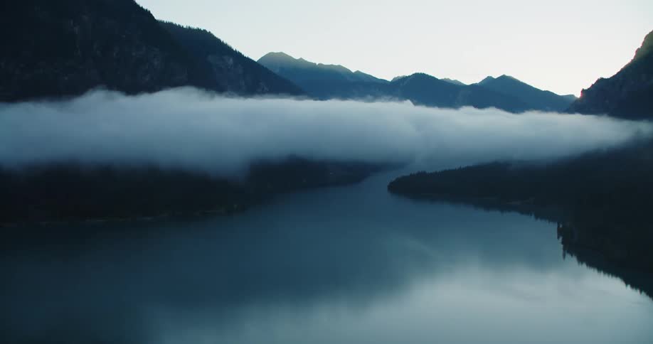 A low cloud floats over a river through a mountain valley during the day