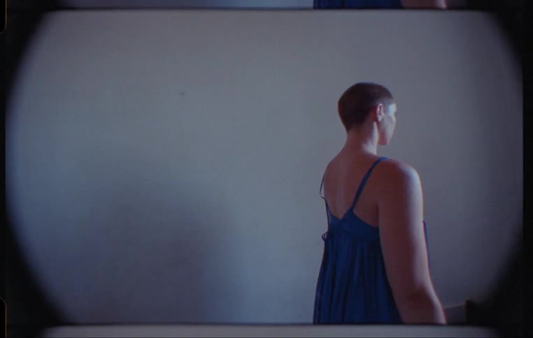 Footage of a woman wearing a dress and standing in a room is displayed