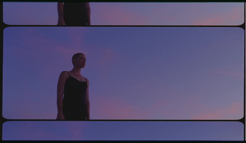 A young woman in an evening dress stands motionlessly outdoors at sunset