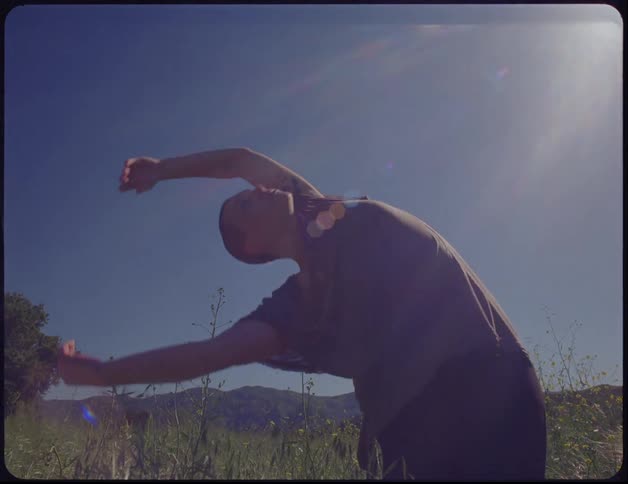 Sunlight shines down on a young woman dancing in a field of grass