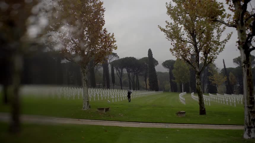 A person holding an umbrella stands in a cemetery of white crosses
