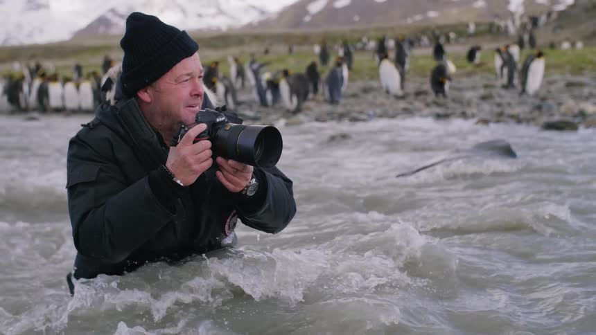 A photographer standing in a fast moving river raises his camera to take a photo