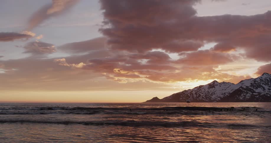 An ocean with waves with a mountain range the sky and clouds in the background
