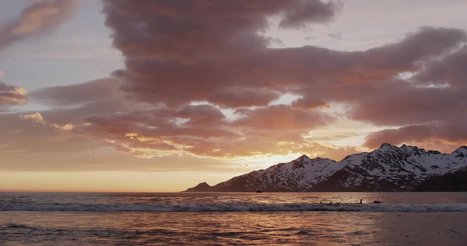 Oceans waves into the beach under a snow capped mountain in the evening