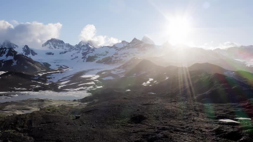 Bright sunlight shines down on a snowy mountain range