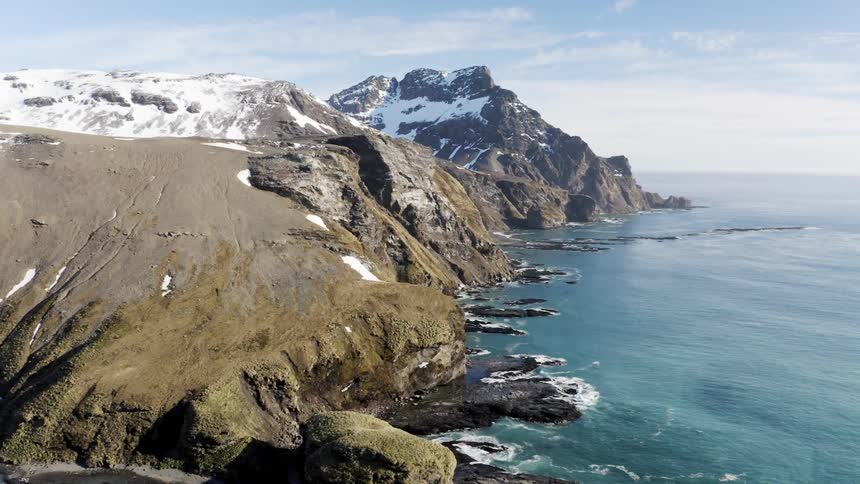 Snow covers mountain slopes near ocean on cloudy day