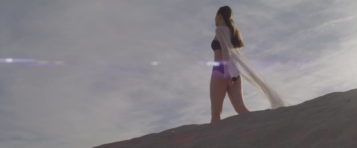 Asian woman with a black bikini and a white transparent dress walks across the beach