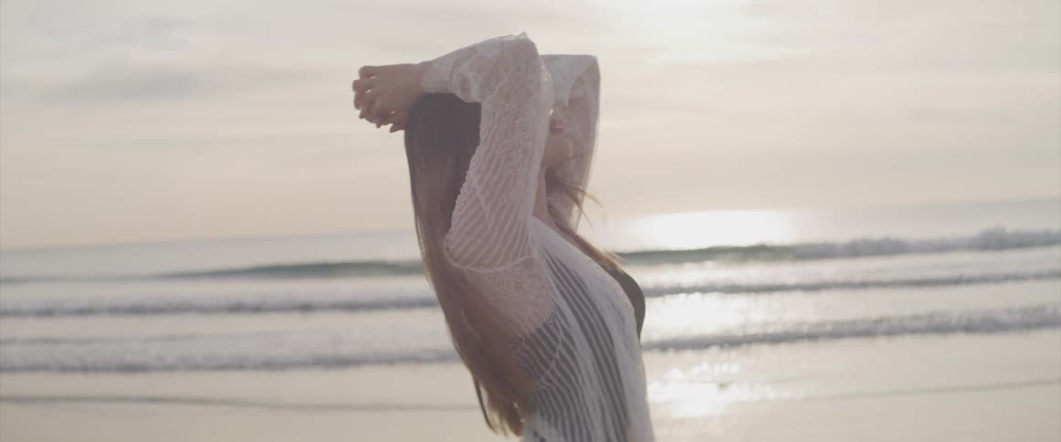 Young woman standing on the sand beach at sunset next to the ocean