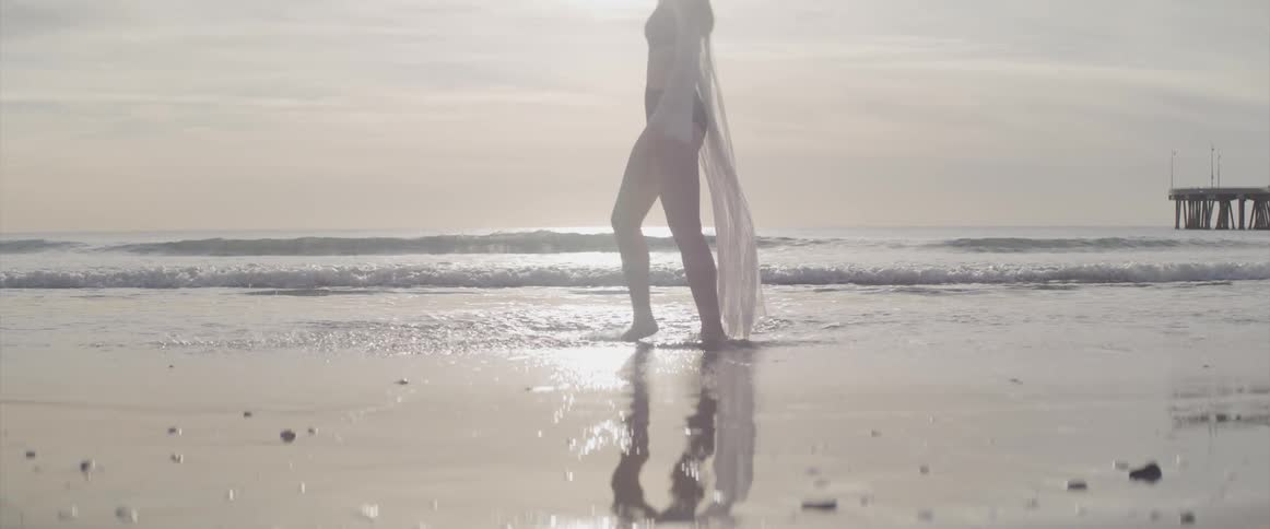 Young woman splashing water with her feet on the white sand beach at sunset next to the ocean