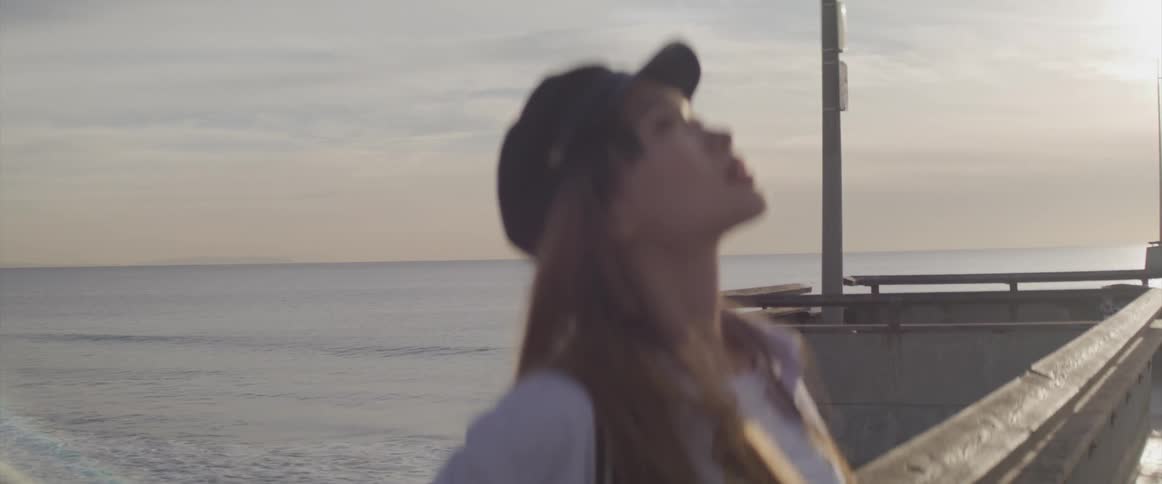 A young woman looks upwards as she leans against the railing on a pier