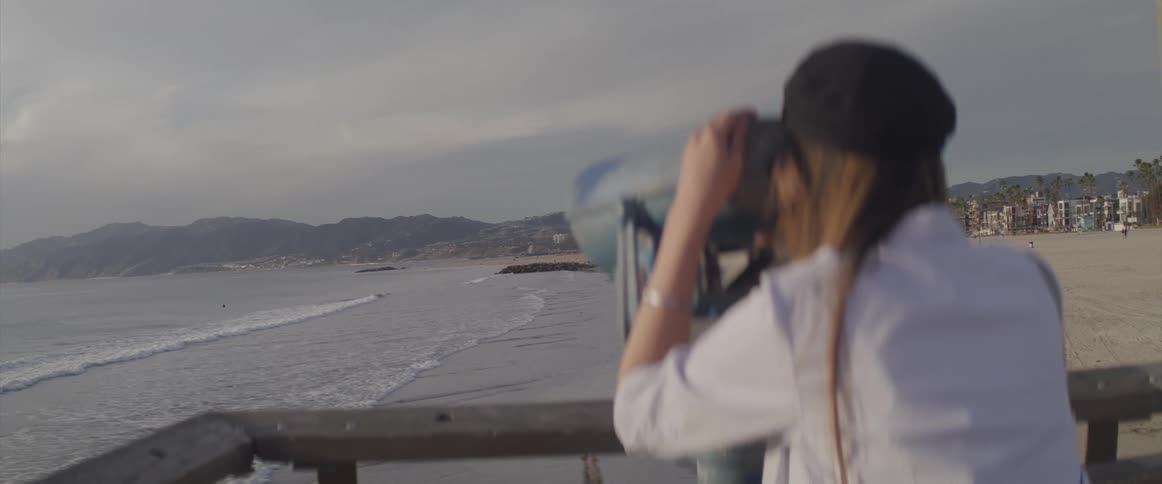 A woman laughs as she stands on a pier and uses a telescope to look at the ocean