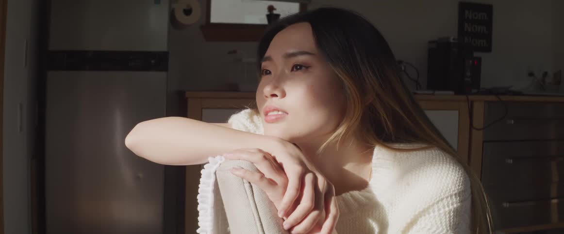 A young woman at home leans her head against a chair and looks off in to the distance