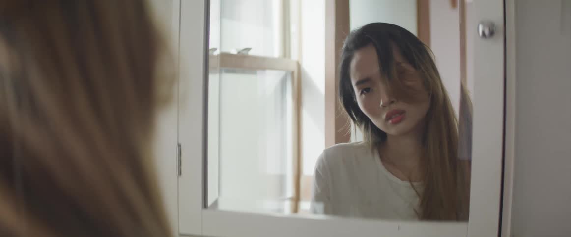 Asian woman with brown hair and a sweater looks in the mirror
