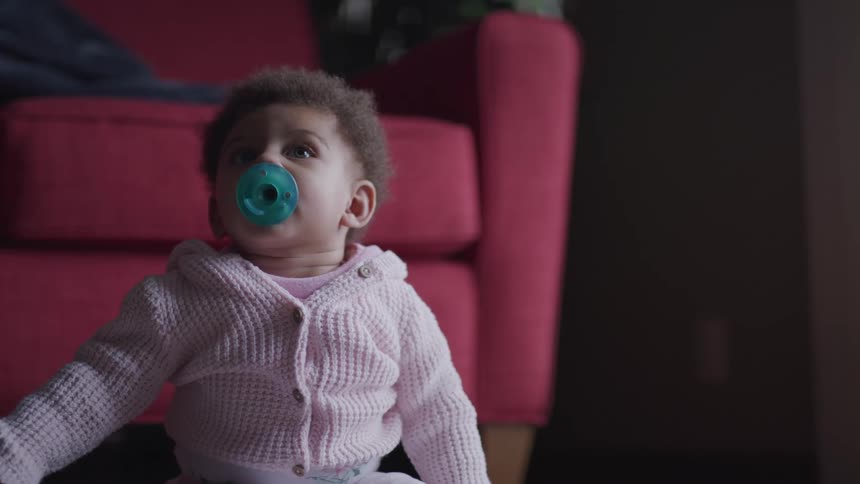Baby with a pacifier sitting on floor in front of red chair