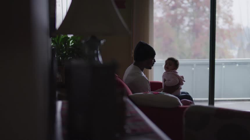 A young father holds and kisses his very cute baby as he sits on a couch
