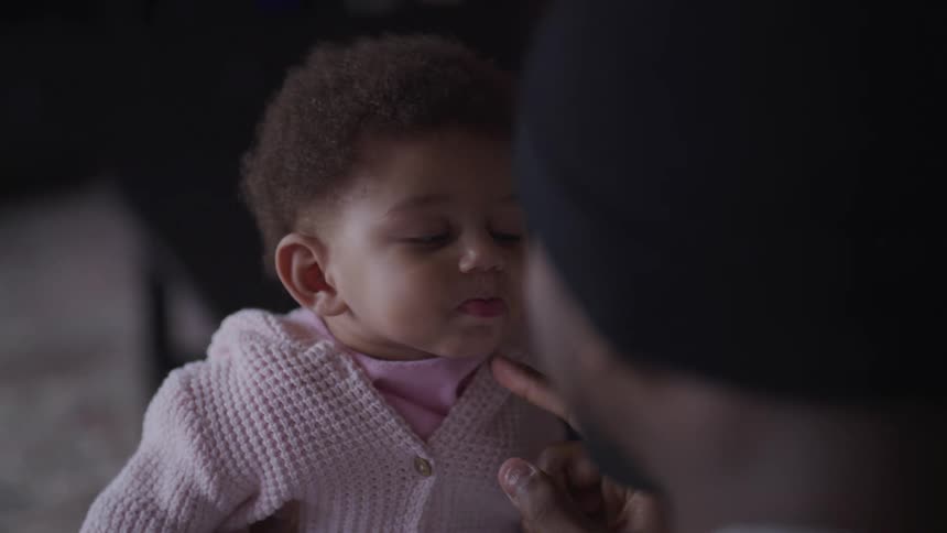 A man with a hat holding and touching a baby with a pink sweater