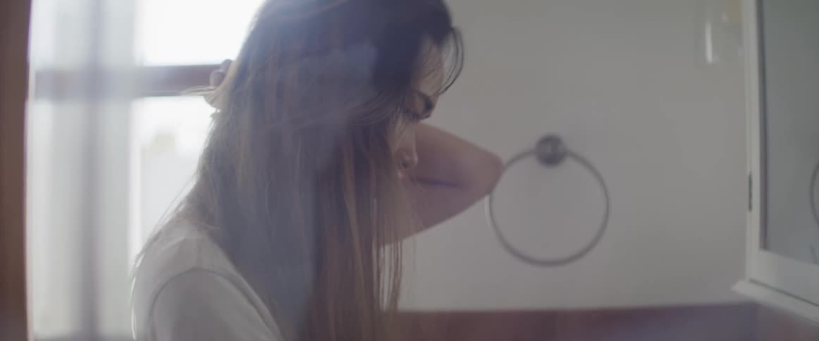 Young woman looks at herself in a mirror on the batroom at home