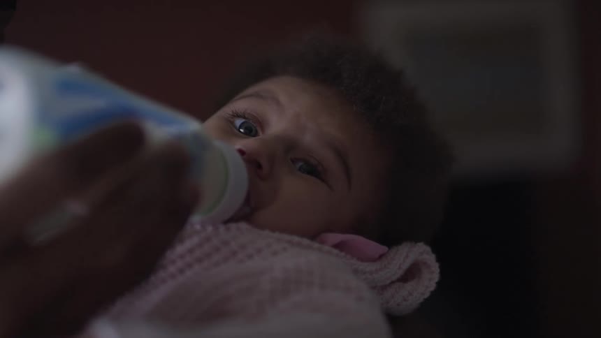An adult feeds a small baby with a bottle