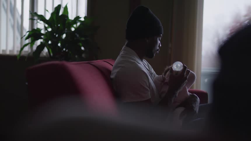 A man sits on a couch and feeds an infant with a bottle