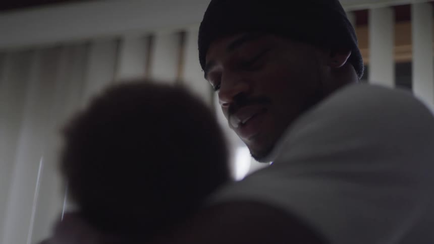 A young man cradles his infant daughter in his arms while gently rocking her