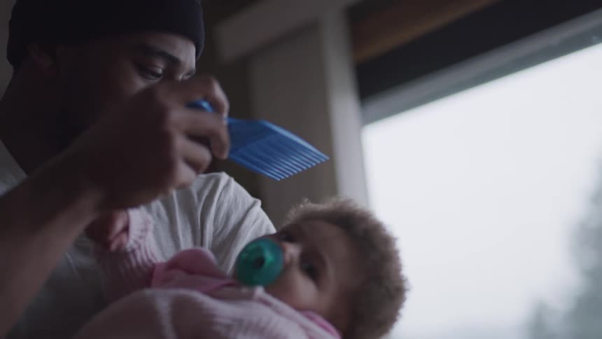 Father holding infant daughter gently combs her hair