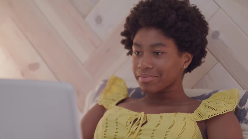 A teenage girl sitting in her bed looking at her laptop