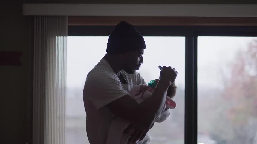 A man with a hat holding a baby and combing her hair with a comb