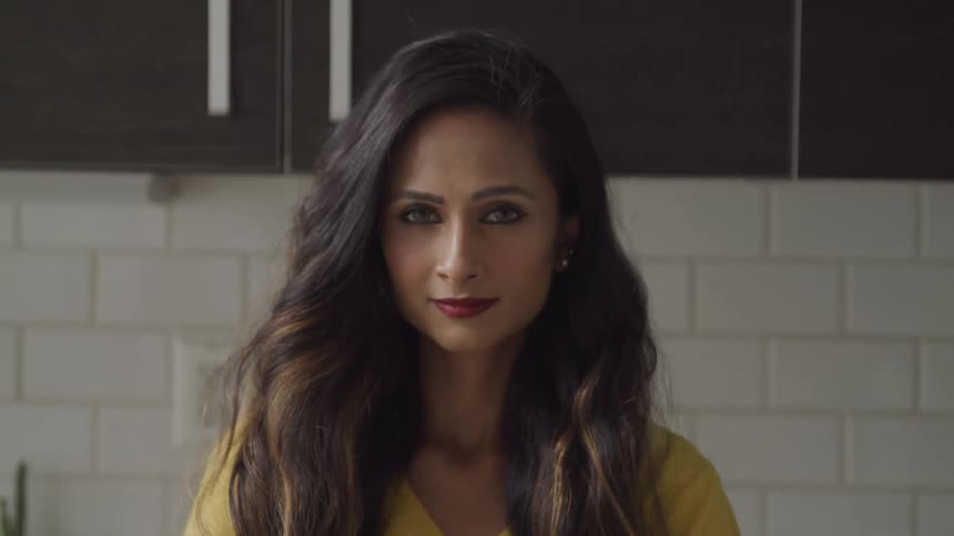Brunette woman with wavy hair and makeup faces the camera with eye contact