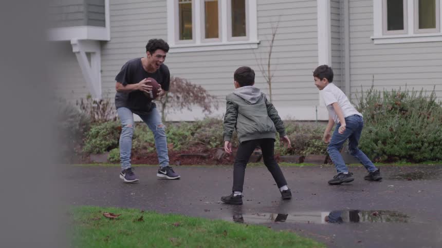 A teenage boy plays football with two younger boys