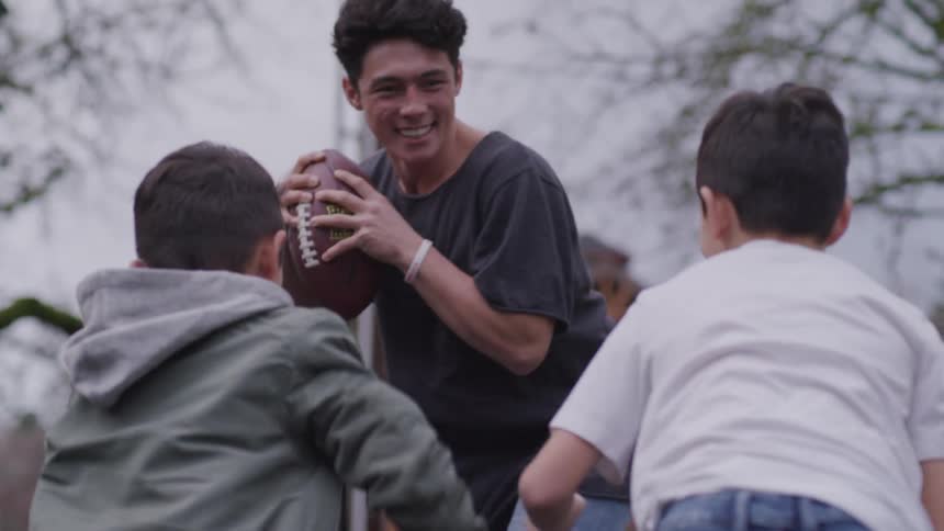 A teenager and his younger brothers play football in their backyard