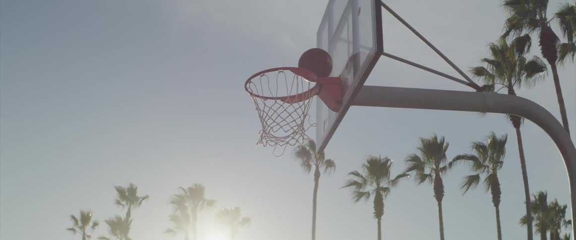 A man performs a layup on an outdoors basketball hoop on a sunny day