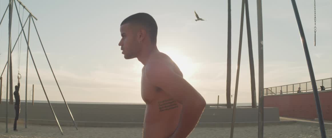 Bare chested man rests after exercising in park on beach
