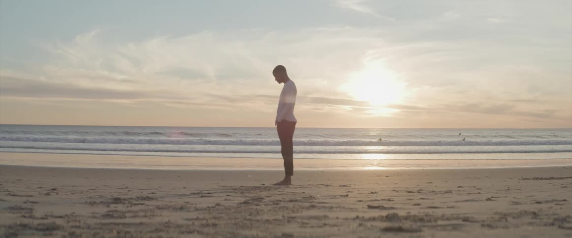A man is standing on the beach at dusk