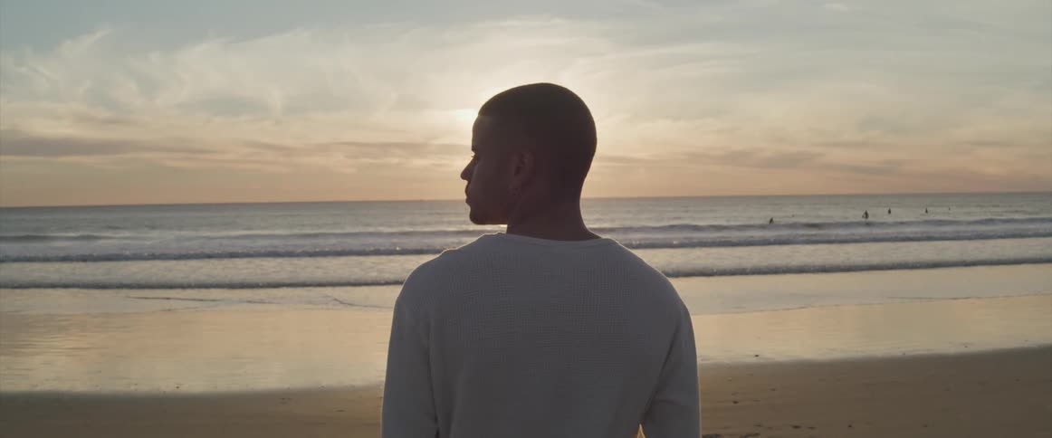 Man with a white sweatshirt looks to the left on the beach at sunset