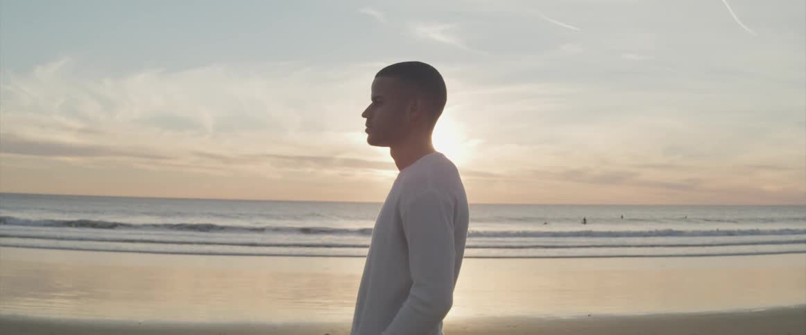 A man is standing by the beach at sunset