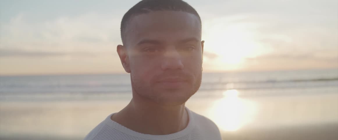 Young man turns to camera and smiles on beach at sunset