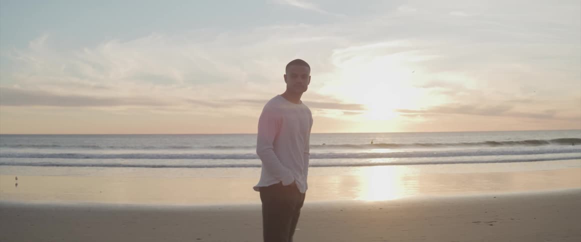 A man stands on a sandy beach with rolling waves