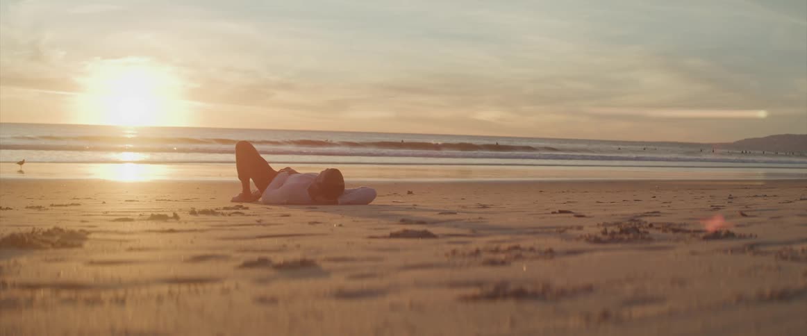A man lying on the beach as the sun sets
