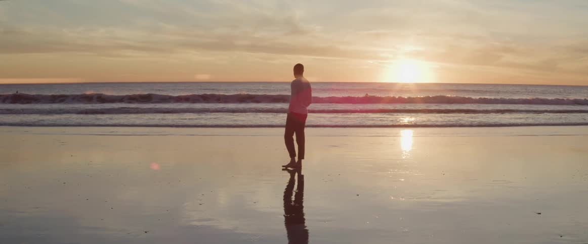 A silhouette of a man walking on the beach with the ocean and sunset in the background