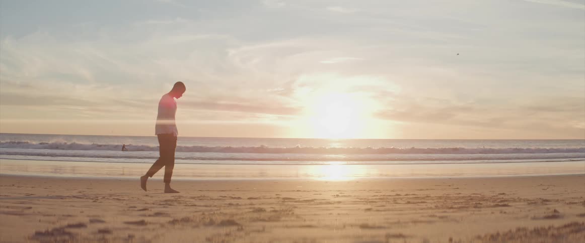 Man walks barefoot along the beach at sunset next to the sea