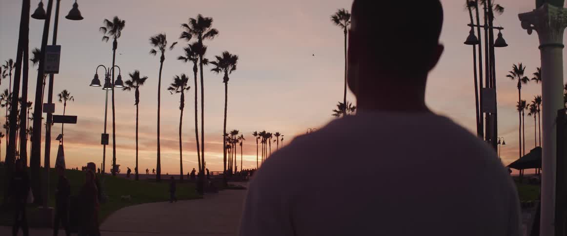 Man stands looking out over park as people walkpast under a red sky