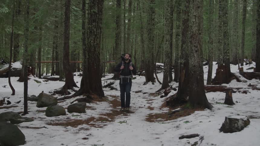A man is backpacking through the woods in winter