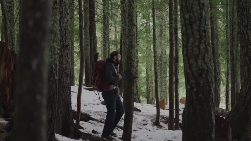 Man with a beard and a red backpack walks down in the snowy forest