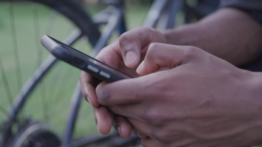 Black mans hands text on smartphone next to a bicycle