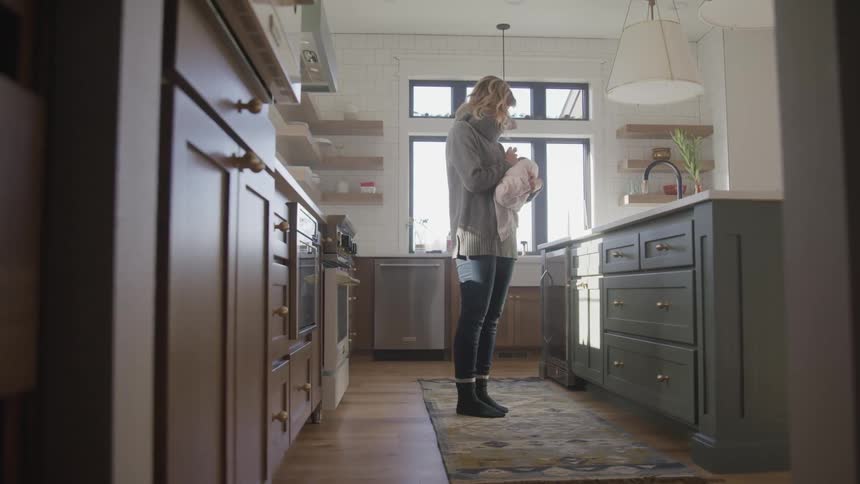 A woman standing in her kitchen feeds her baby
