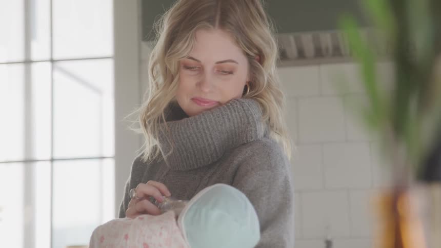 A white mother smiles as she gives her baby a bottle