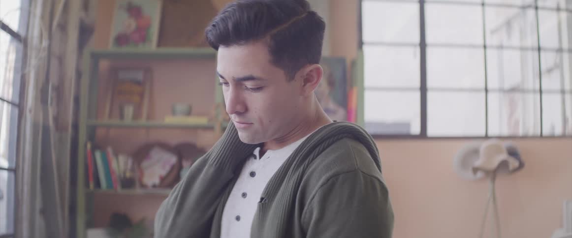 Man wearing a gray hoodie and looking downwards tilts his head up and looks sad
